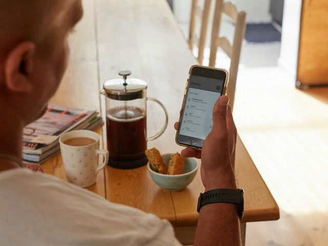 Mann am Frühstückstisch schaut auf sein Handy mit Blutzucker-Messdaten