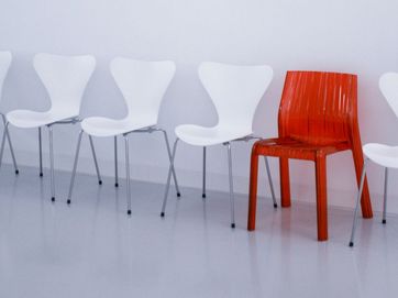 Roter Stuhl zwischen weißen Stühlen