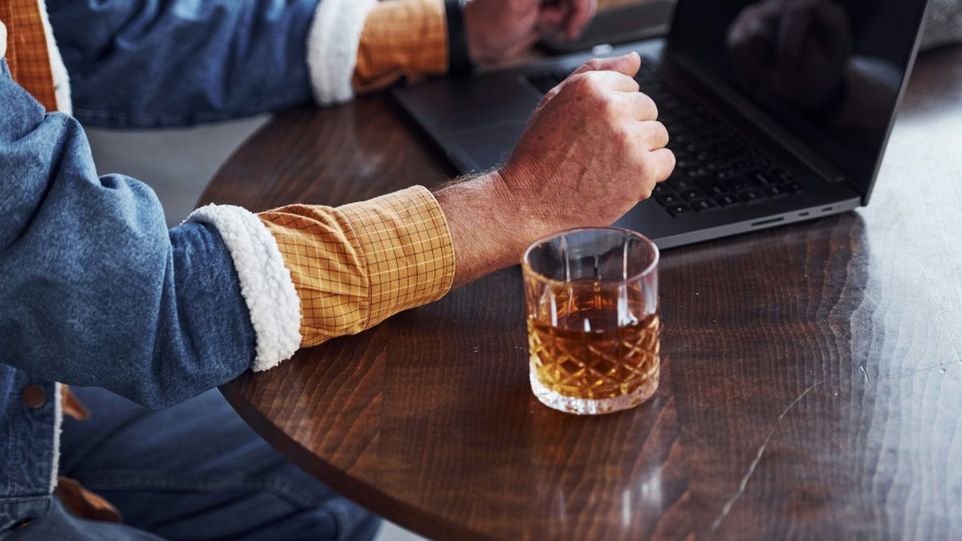 Glas Whisky neben Laptop