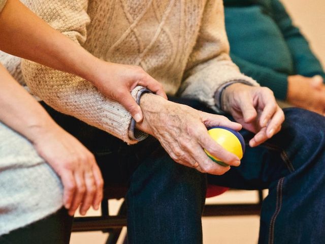 Ältere Person, die einen Stressball hält und von Pflegekraft unterstützt wird.