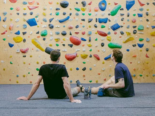 Zwei Männer sitzen vor einer Boulderwand und ruhen sich aus