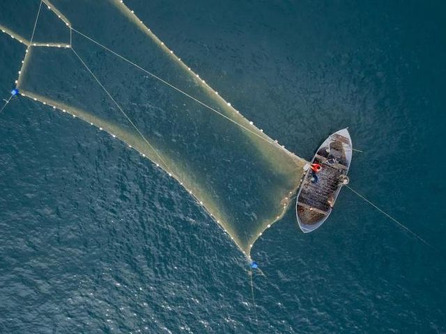 Kleines Fischerboot mit großem, ausgeworfenen Fangnetz 