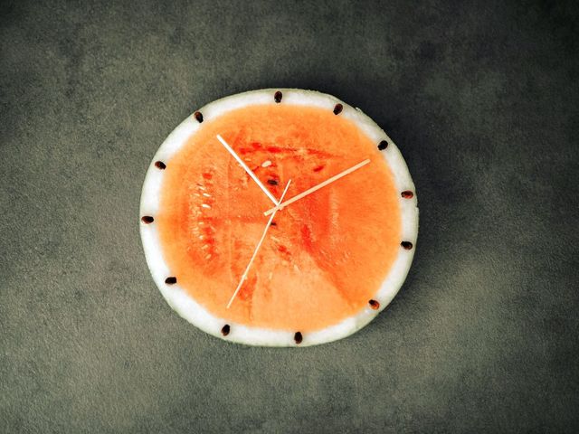 Aufgeschnittene Melone, mit Holzzeigern als Uhr drapiert.
