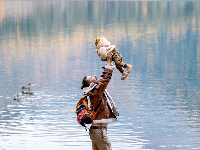 Ein Mann hebt ein Kleinkind hoch, im Hintergrund ein See mit Enten
