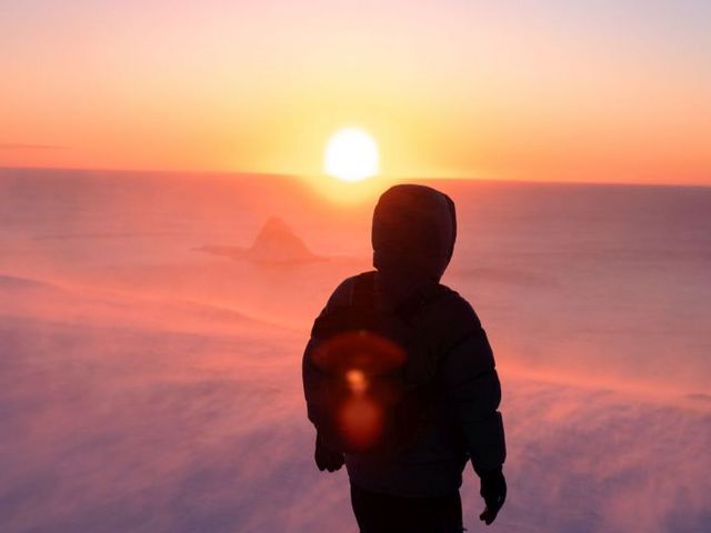 Rückenansicht eines Mannes in Schneelandschaft mit Blick in die Sonne