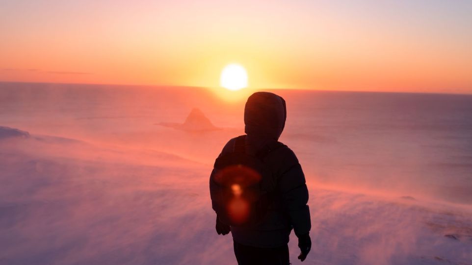 Rückenansicht eines Mannes in Schneelandschaft mit Blick in die Sonne