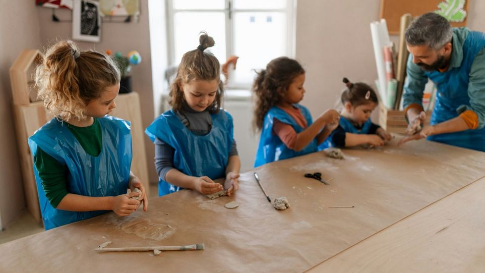 Vier Kleinkinder kneten Ton, angeleitet von einem Erzieher