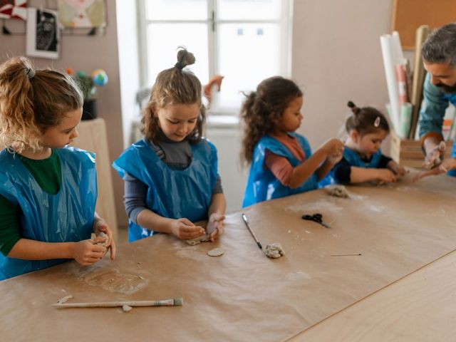 Vier Kleinkinder kneten Ton, angeleitet von einem Erzieher