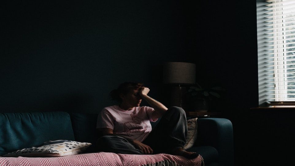 Frau mit traurigem Gesichtsausdruck, die sich auf ein Sofa kauert, Gesicht in die Hand gestützt