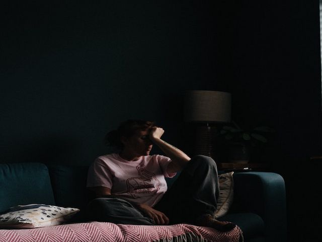 Frau mit traurigem Gesichtsausdruck, die sich auf ein Sofa kauert, Gesicht in die Hand gestützt