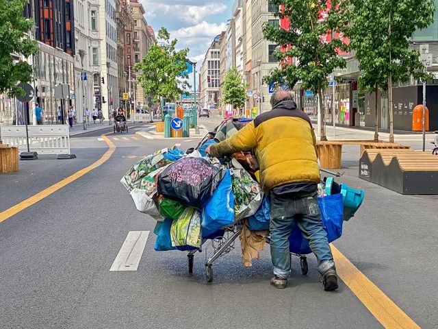 Mann schiebt sein Hab und Gut in einem Einkaufswagen voller Plastiktüten durch eine Geschäftsstraße