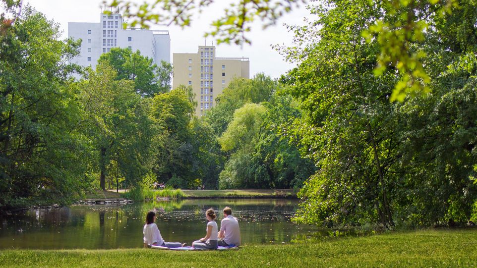 Drei Menschen sitzen am See im Park. 