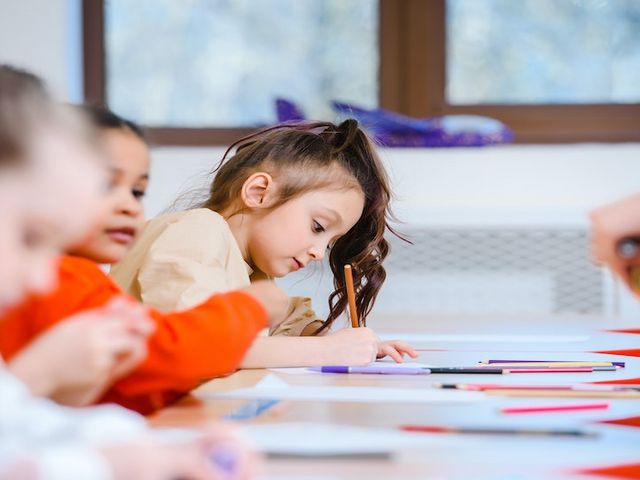 Drei Mädchen sitzen in einem Klassenzimmer, auf den Tischen vor ihnen liegen Stifte und Papier.
