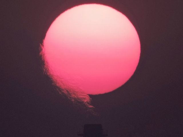 Rötliche Sonne mit Rauch aus Schornstein im Vordergrund