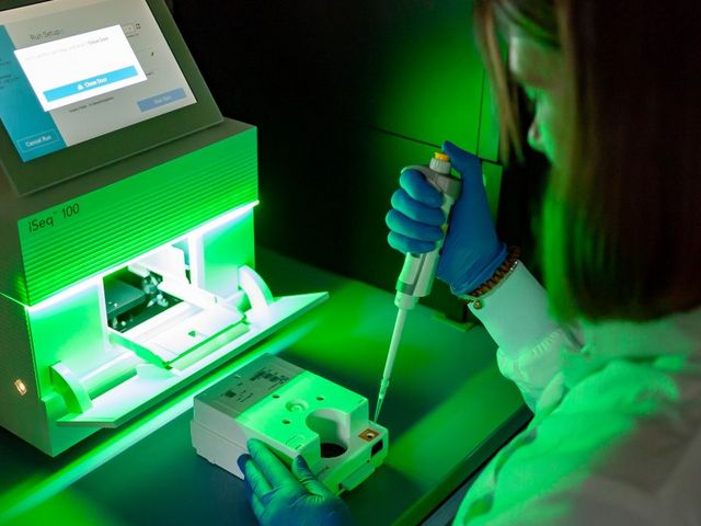 Wissenschaftlerin mit Pipette vor Genomsequenzierungs-Apparat